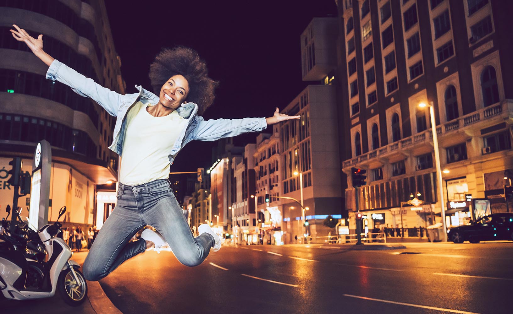 Beautiful young black woman jumping in a city street at night