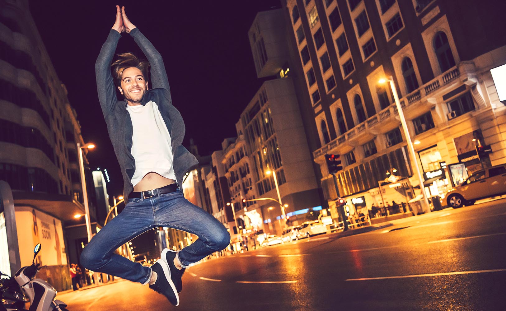 Attractive young caucasian man jumping in a city street at night