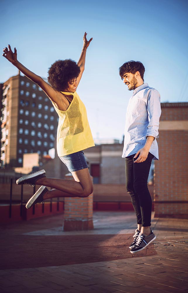 Young multirracial couple jumping happy at sunset on the rooftop
