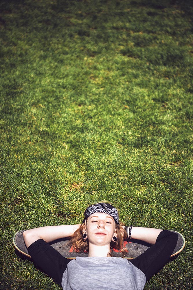 Young woman resting in the grass after practicing skateboard