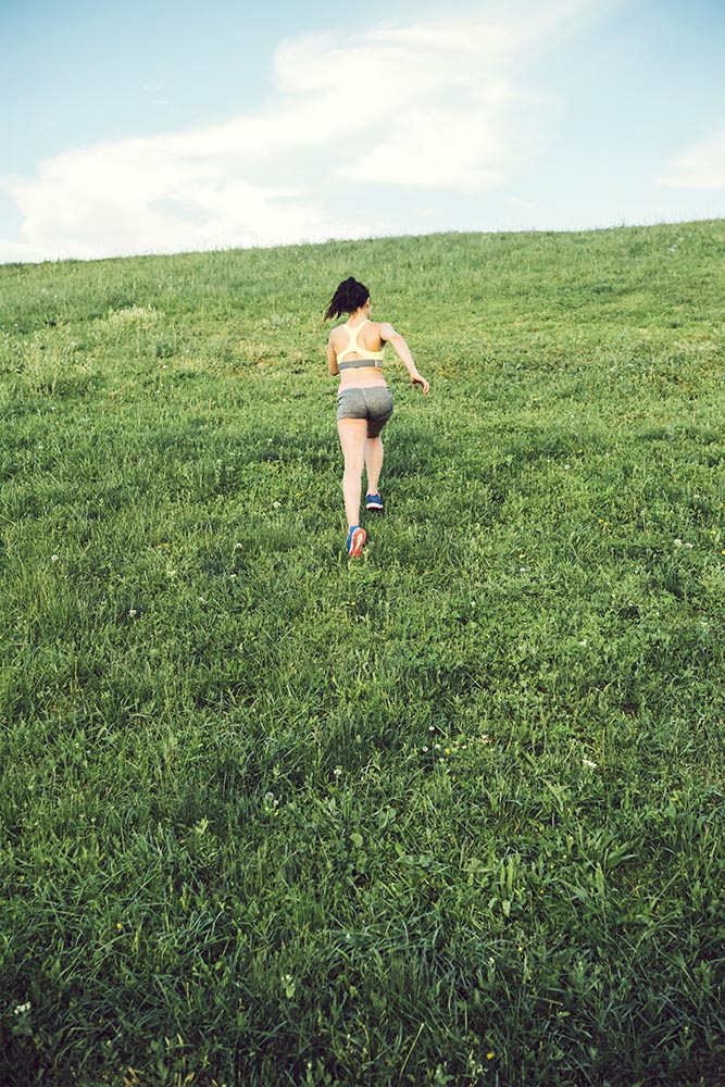 Sporty woman running over a small hill against the skyline