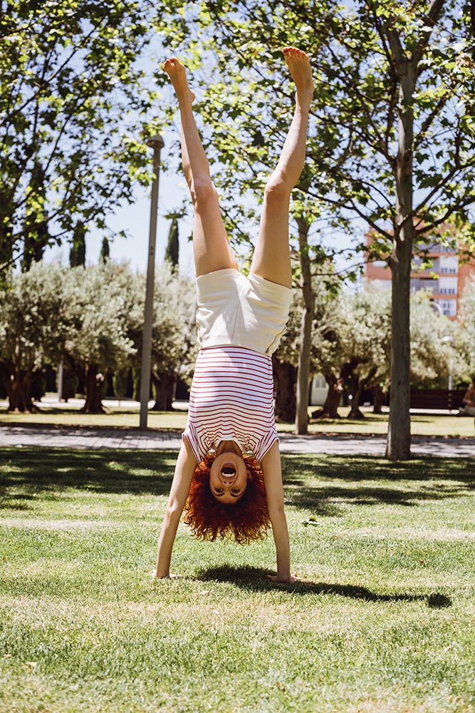 Funny young Woman doing handstand in park in summer