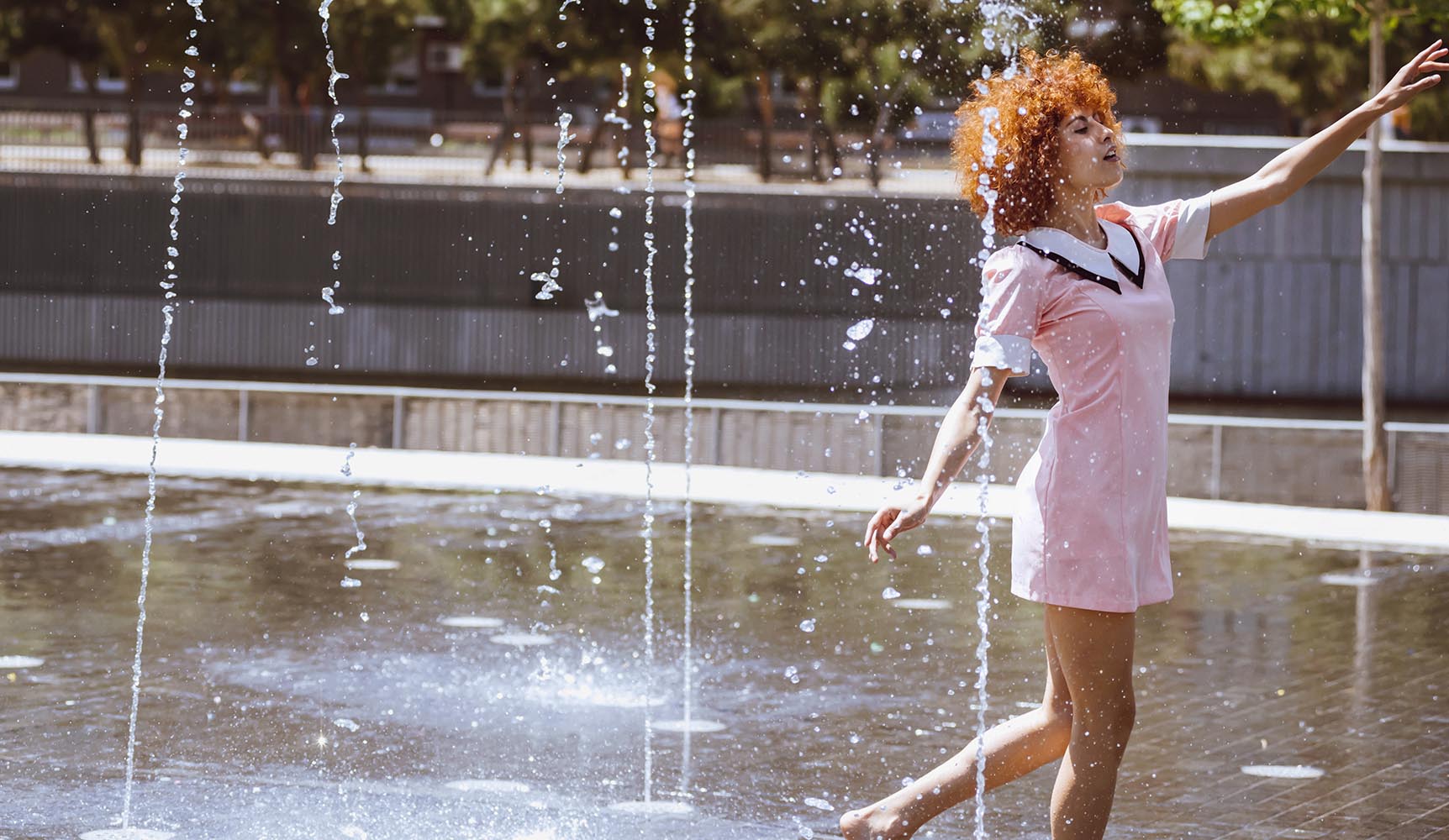 Young beautiful brunette woman playing at outdoor water fountain
