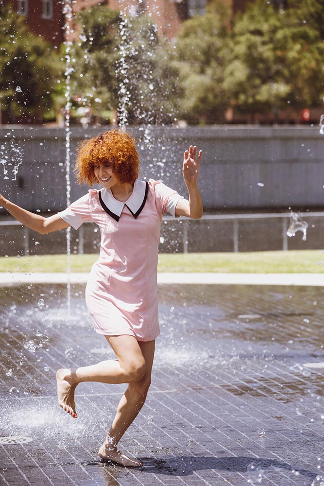 Young beautiful brunette woman playing at outdoor water fountain