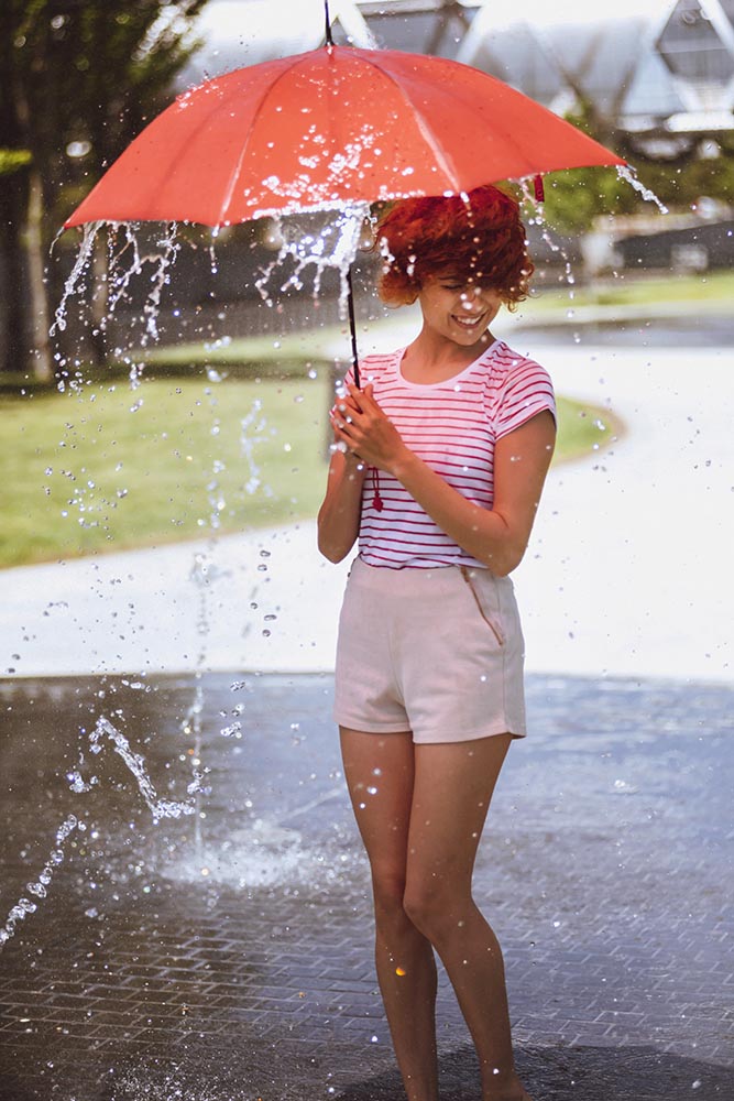 Young beautiful woman playing at outdoor water fountain with an