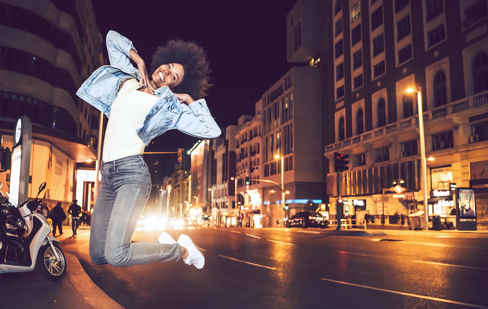 Beautiful young black woman jumping in a city street at night
