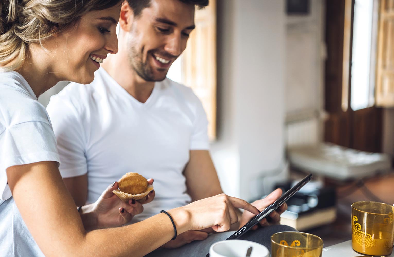 Laughing young couple using tablet at breakfast