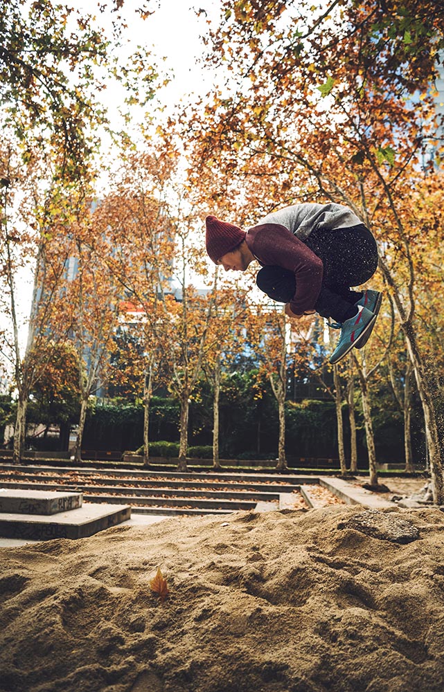 Man jumping above sand pile in park