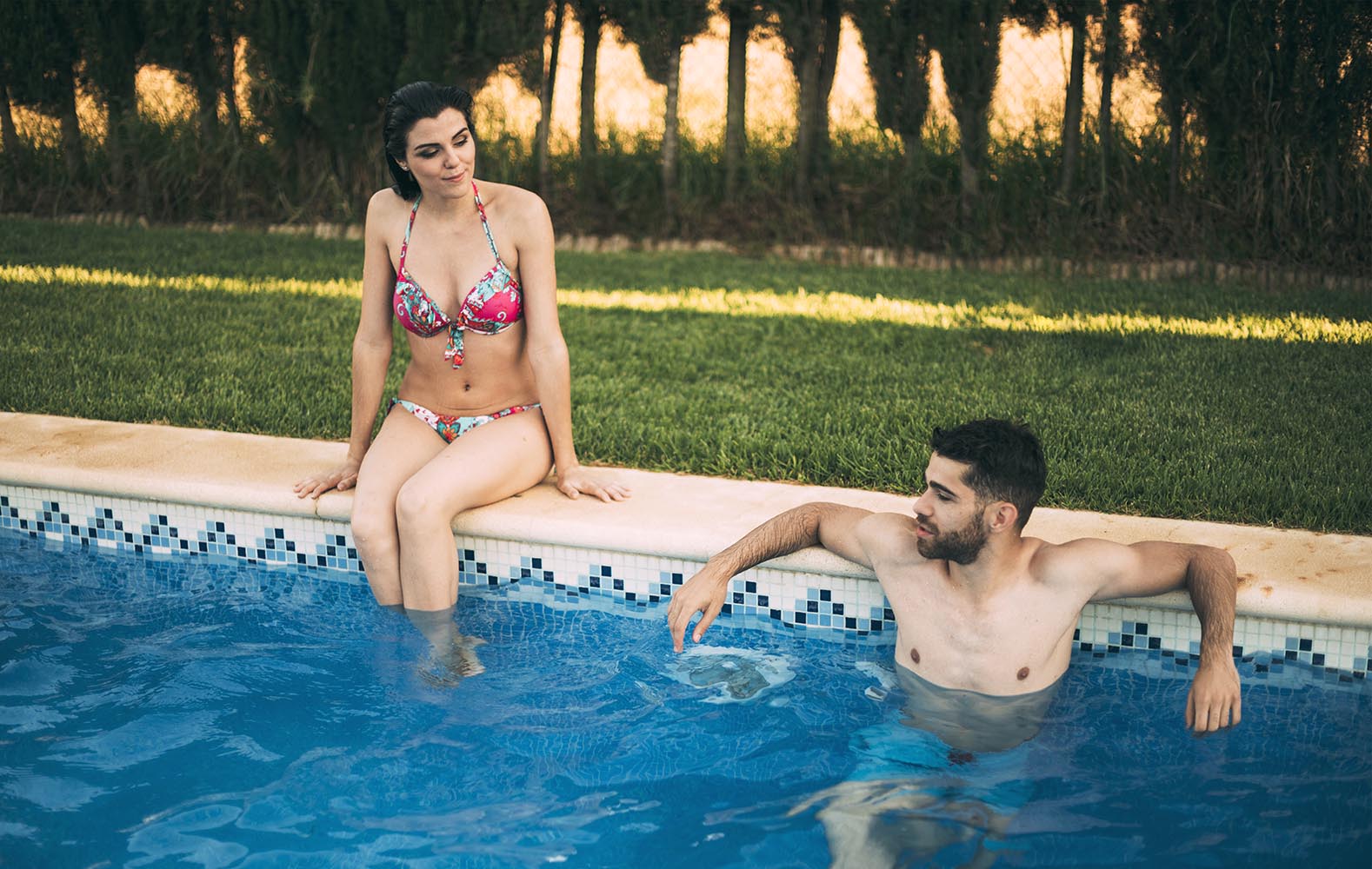 Guy swimming and girl sitting on poolside